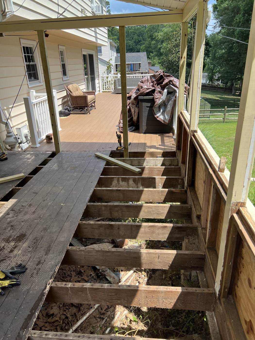 A deck mid-replacement with old wood boards removed, framing exposed, and new decking installed on the far section
