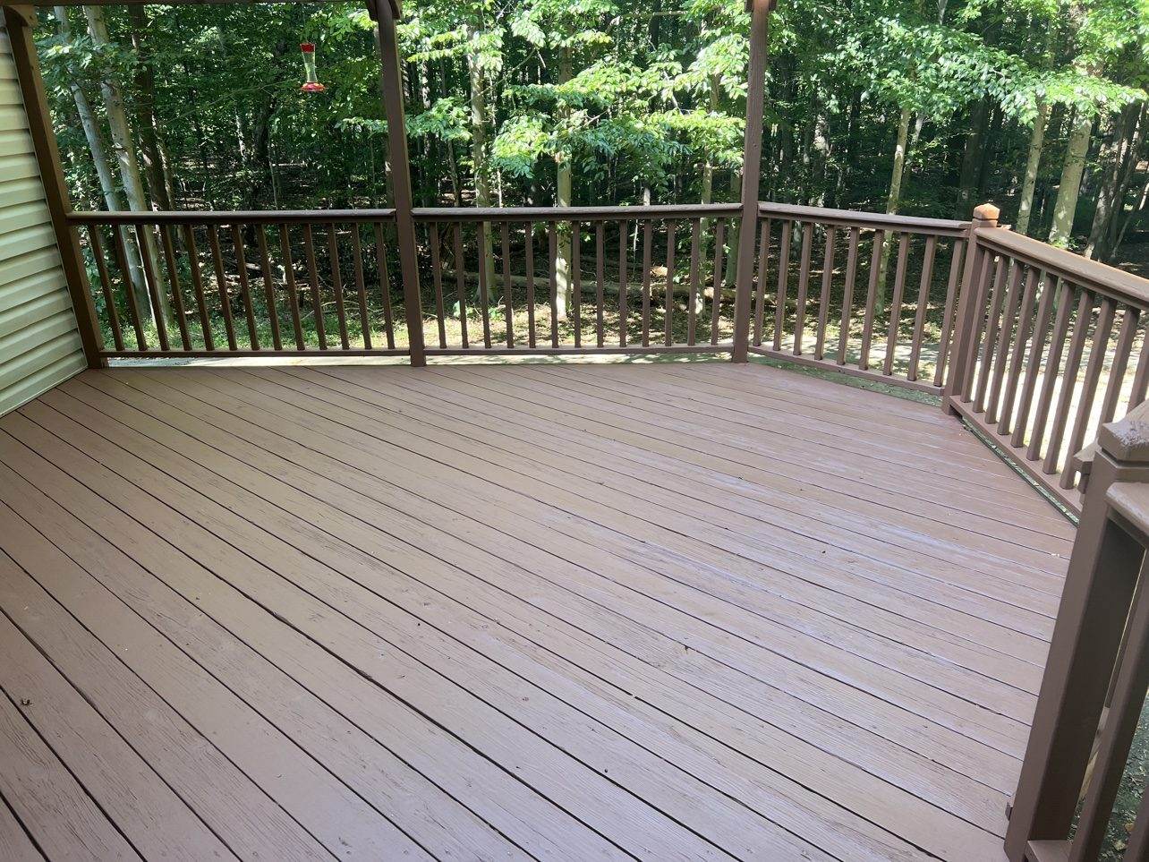 A finished pressure-treated wood deck with solid-color brown stain and matching railing, overlooking woods