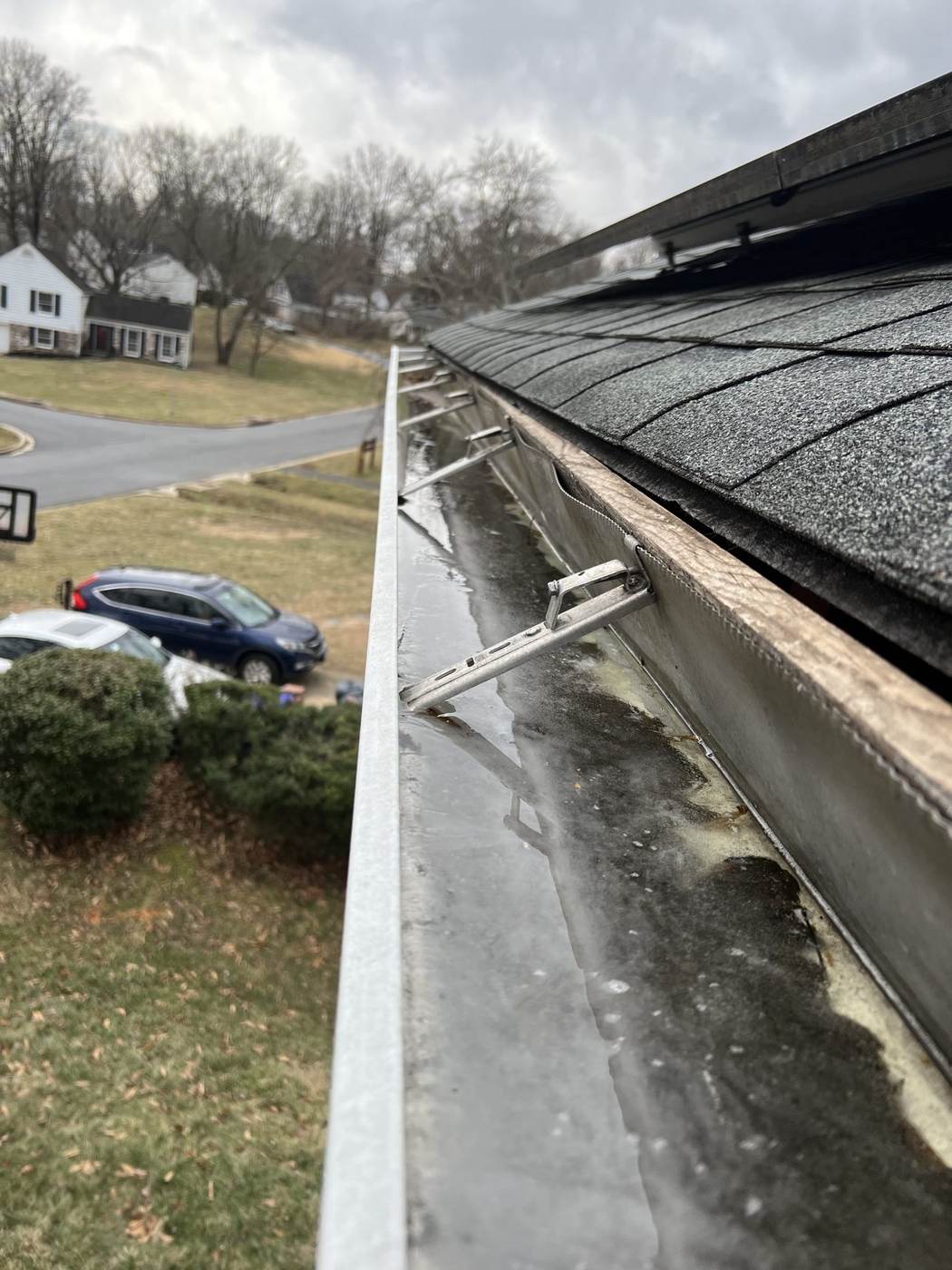 A gutter on screwed hangers with ice and debris along the shingle edge — hardware built to survive Maryland winters.