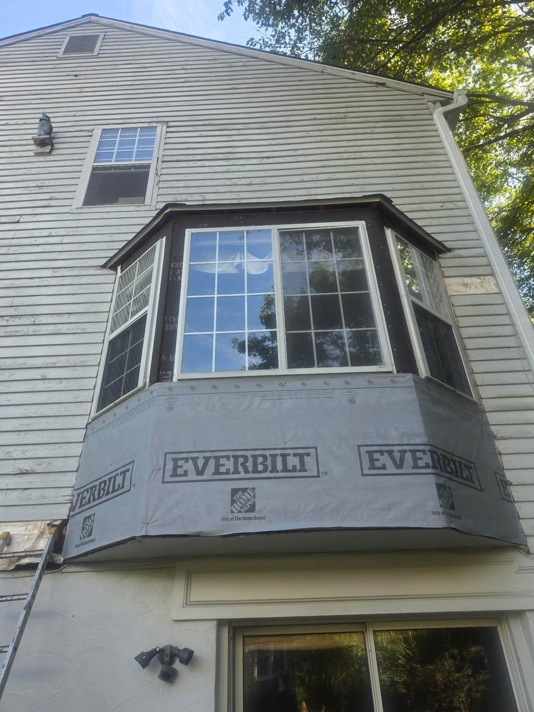 A bay window siding repair in progress — siding removed, house wrap installed underneath before new panels go up.