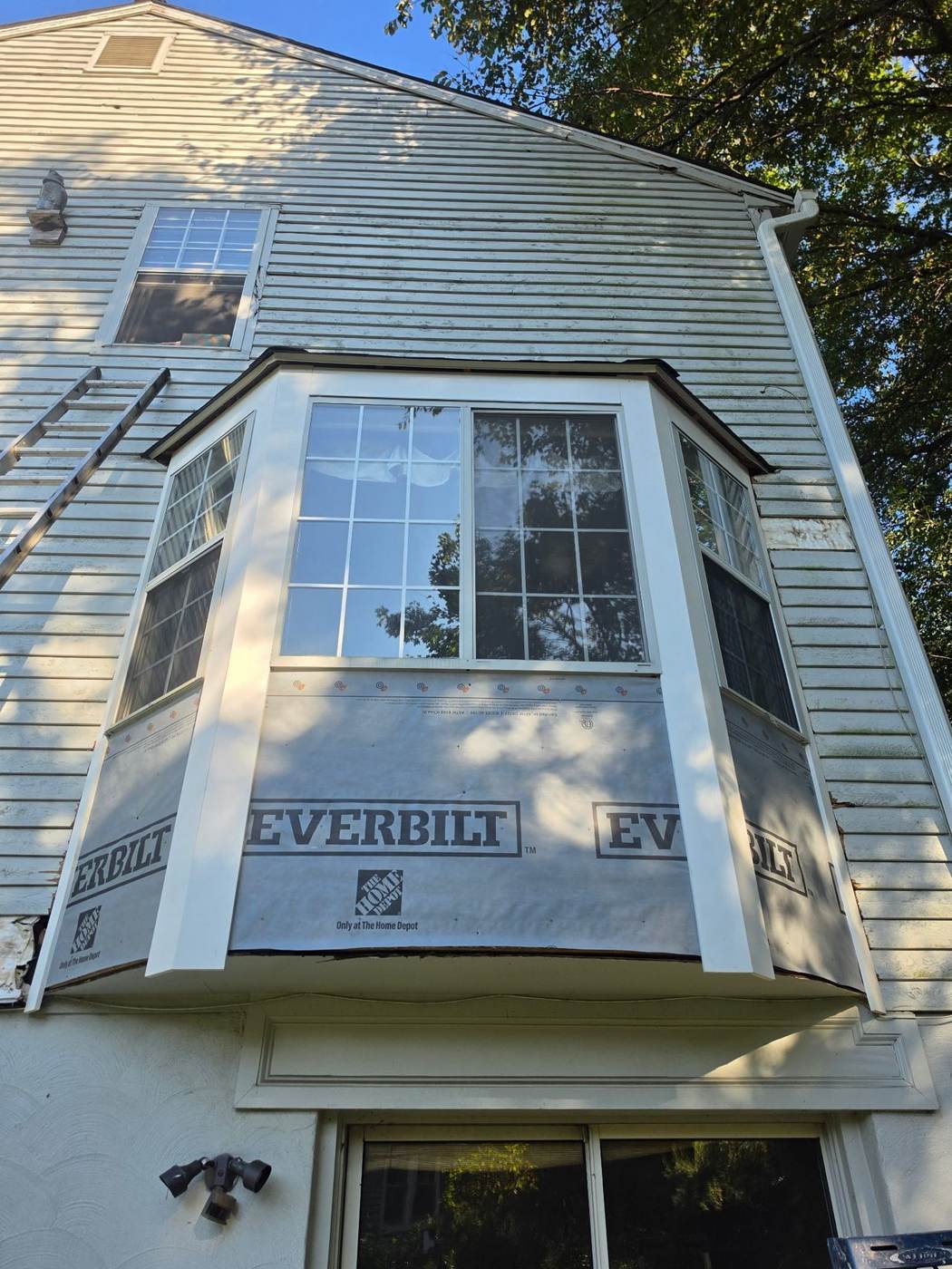 The same bay window repair further along — white corner boards installed over the house wrap, ready for siding.